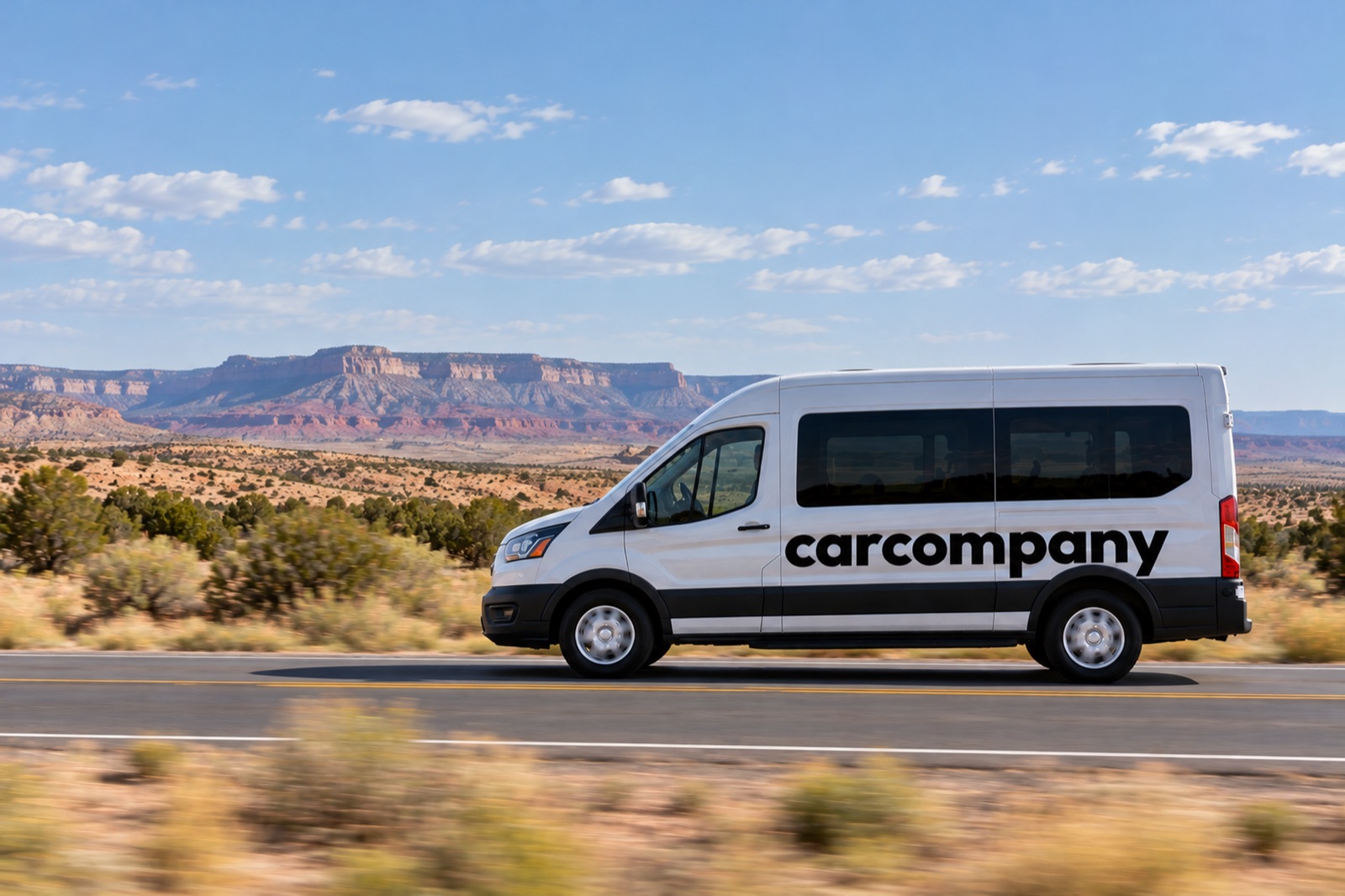 A white CarCompany passenger van on a desert highway, red rock mesas and a blue sky behind it.